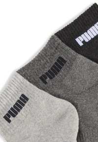 Trzy pary skarpet w różnych odcieniach szarości i czerni, z prążkowanymi mankietami oraz logo "PUMA" w kontrastujących kolorach.