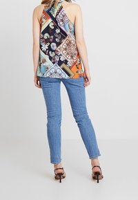 Top senza maniche multicolore con un design a patchwork in vari motivi floreali e geometrici, abbinato a jeans dritti classici blu chiaro.