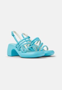 Une paire de sandales bleu clair avec plusieurs brides croisées, un talon bloc conturé et une finition lisse et brillante.
