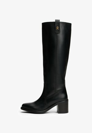 Black mid-calf leather boot with block heel and gold emblem on pull tab, smooth finish, rounded toe, side stitching, and slightly raised sole.