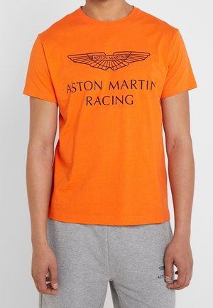 Oranges Baumwoll-T-Shirt mit schwarzem "ASTON MARTIN RACING" Logo und Flügelgrafik in der Mitte, kurzen Ärmeln und Rundhalsausschnitt.