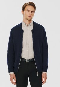 Granatowy kardigan na zamek błyskawiczny z żeberkowym dekoltem, wykonany z miękkiego materiału dzianinowego. Posiada gładki zamek oraz kontrastowe, jasne podszewkę.