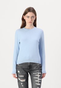 Lys blå langermet genser i mykt strikket stoff, med rund hals og ribbestrikket kant, sammen med slitte grå jeans.