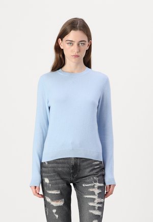 Lys blå langermet genser i mykt strikket stoff, med rund hals og ribbestrikket kant, sammen med slitte grå jeans.