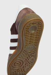 Sneaker in camoscio marrone con strisce bianche, suola in gomma con motivo a rilievo e logo visibile sulla suola esterna.