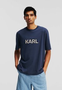 T-shirt à manches courtes bleu marine avec un logo "KARL" en broderie grise. Tissu doux avec une coupe décontractée.