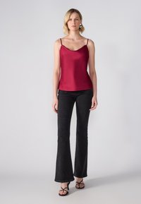 Camisola di raso borgogna con scollatura a barca e spalline sottili, abbinata a jeans neri a palazzo e sandali neri con cinturini.
