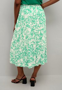 Kvetinová sukňa v zelenej a bielej farbe, s plným dizajnom, elastickým pásom a mäkkou tkaninou. V kombinácii s čiernymi sandálmi na blokovom podpätku so šnúrkami.
