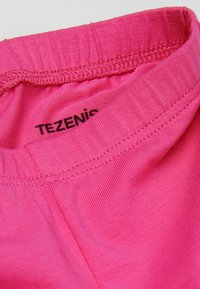 Detailní záběr na pás prádla v růžové barvě, který ukazuje elastické švy a částečně viditelnou černou značkovou štítek "TEZENIS".