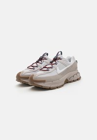 Sive tenisice za sport s teksturiranom gornjištem, gumene potplate i crvenim detaljima. Imaju sistem vezanja i Nike logo sa strane.