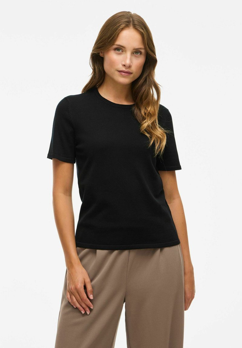 Juodas trumpomis rankovėmis marškinėliai, pagaminti iš minkštos medžiagos, su apvaliu kaklu ir laisvu fasonu. Dėvimi su smėlio spalvos, aukštu liemeniu kelnių.