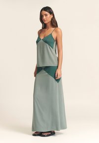 Sada zo zeleného hodvábneho tielka a maxi sukne s geometrickým farebným blokovým dizajnom, nastaviteľnými ramienkami a hladkou textúrou.