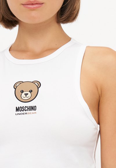 Biely bezrukávový top s kreslenou medveďou nálepkou a textom "Moschino UNDERBEAR" pod ňou. Mäkká tkanina s hladkou textúrou.