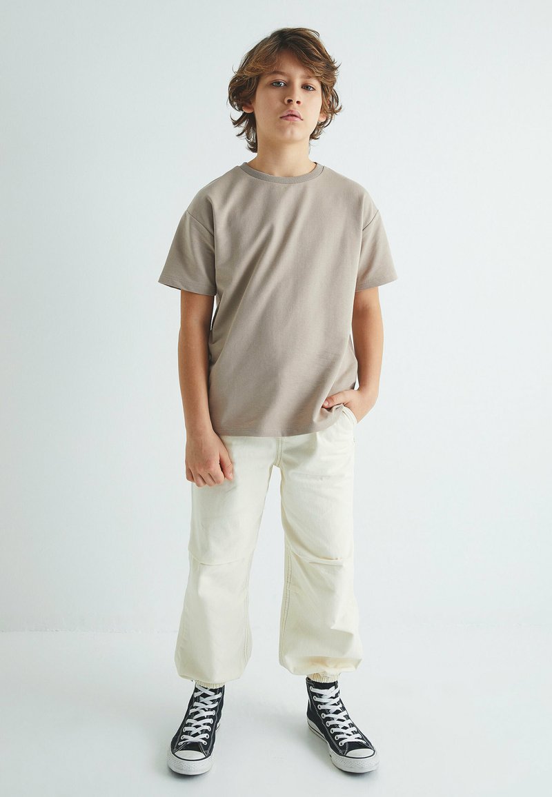 Beige t-shirt med korte ærmer og rund hals, parret med cremede, tætsiddende bukser og sorte højtop sneakers.