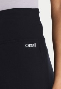 Crne Leggings visoki struk s glatkom teksturom, s bočnom džepom i bijelim "casall" logom na struku.