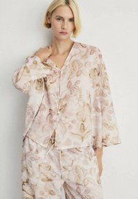 Ensemble de loungewear léger à motif floral dans des tons de rose doux et de beige. Présente un décolleté en V, des manches longues et des accents de boutons.