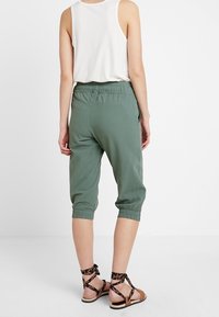 Pantalones cortos de color verde oliva con una cintura elástica, tobillos ajustados y un corte relajado, combinados con sandalias marrones con tiras.