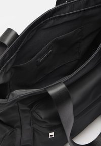 Black fabric tote bag interior with a soft texture, features a label, a pocket, and a zippered closure. Straps are made of durable webbing.