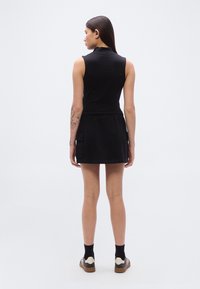 Μαύρο αμάνικο φόρεμα με ψηλό γιακά, ελαστική μέση και πλαϊνές τσέπες. Διαθέτει μινιμαλιστικό σχέδιο και ομαλή υφή.