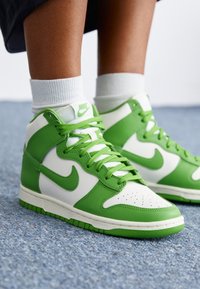 High-top sneakers featuring a green and white leather design. Includes a perforated toe box, green laces, and a rubber sole.