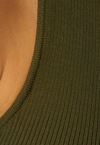 Ribbad linne i olivgrönt, med en rundad halsringning och en mjuk textur. Närbild som betonar sömnadsdetaljer och tygkvalitet.