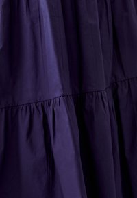 Gonna tiered di un viola scuro, realizzata in tessuto liscio, con cuciture arricciate e un design fluido, caratterizzata da una leggera lucentezza che riflette la luce.