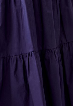 Tumši purpursarkans svārku slāņu, kas izgatavots no gludas auduma, ar savelktiem šuvēm un plūstošu dizainu, ar nedaudz spīguļojošu gaismu.