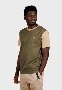 Camiseta de manga corta en verde oliva y beige con un pequeño logo de elefante en el pecho. Hecha de un suave material de algodón.