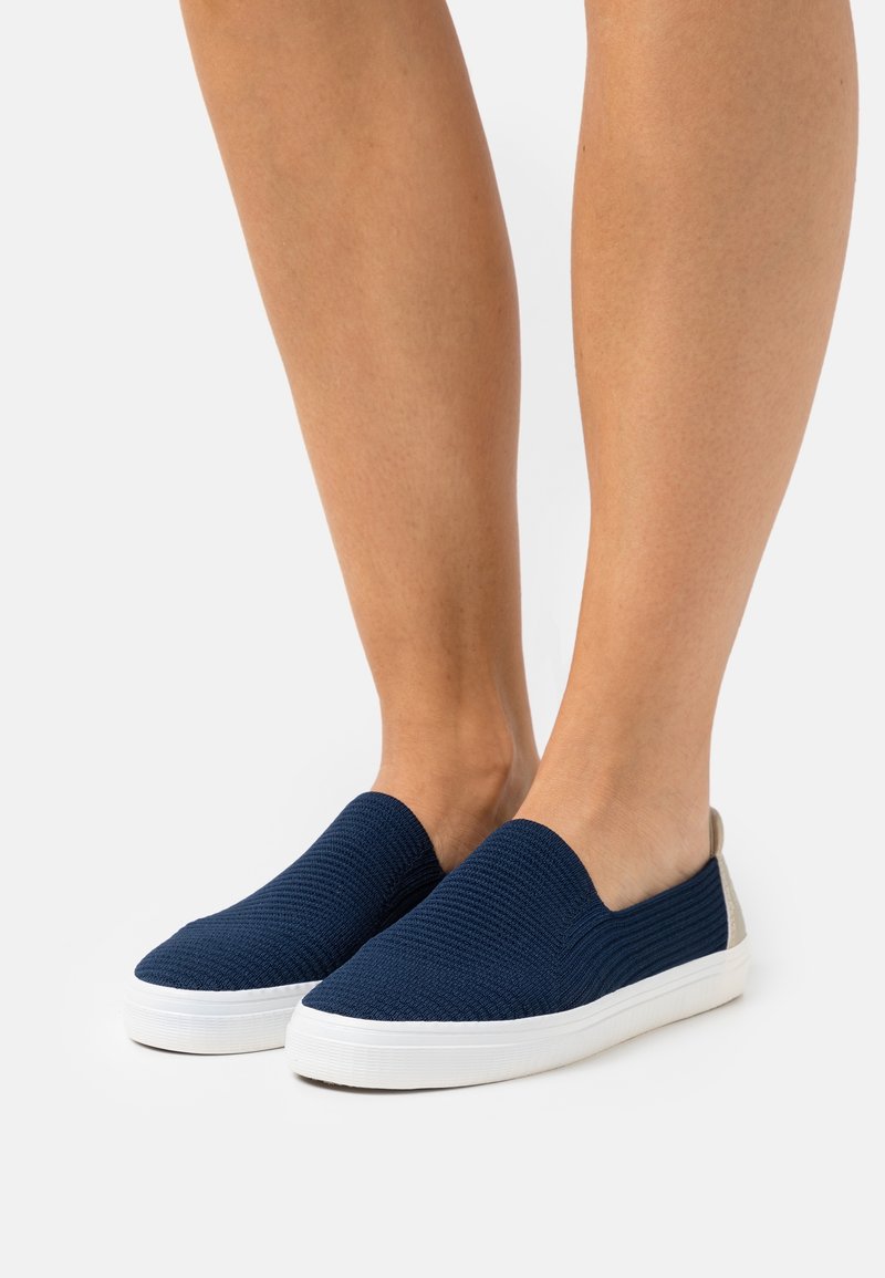 Baskets slip-on navy avec dessus texturé, semelle en caoutchouc blanche et panneau de talon gris clair contrastant. Conçues pour le confort et la facilité de mise en chaussure.