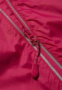 Gros plan sur la fermeture éclair d'une veste rouge avec un tire-zip en tissu et une bande réfléchissante le long de la ligne de zip sur un matériau résistant à l'eau.