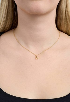 Njegovana ogrlica od zlatnog lanca s malim privjeskom u obliku zvijezde, nošena oko vrata žene na crnoj pozadini majice.