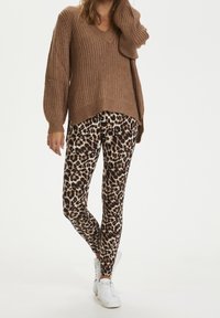 Brun, stickad v-ringad tröja med ribbad textur, i kombination med åtsittande leggings med leoprint i beige, svart och krämfärgad. Vita sneakers.
