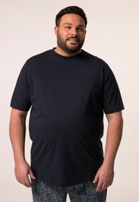Camiseta de manga corta azul marino hecha de tela suave; presenta un logo sutil en el pecho; combinada con pantalones de un tono azul claro y con estampado.