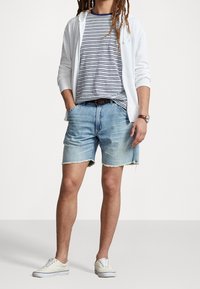 Avslappnad outfit med en vit zip-up huvtröja, en randig t-shirt i marinblått och vitt, ljusblå denimshorts, och vita sneakers.