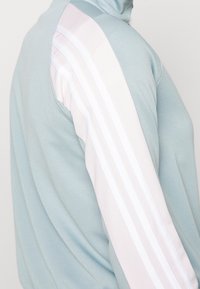 Veste bleu clair avec des rayures verticales rose clair et blanches le long de la manche, vue de côté en gros plan.