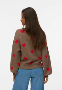 Pull marron avec des motifs de cœurs rouges, manches longues et coupe décontractée. Associé à un jean en denim bleu, modèle montré de dos.