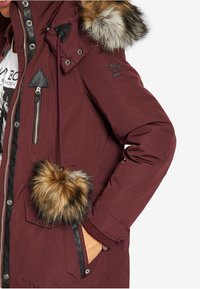 Parka burdeos con detalles de piel sintética en la capucha, que cuenta con bolsillos con cremallera y acentos de cuero. Tela texturizada y puños acanalados.