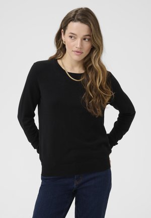 Maglione nero a maniche lunghe in tessuto morbido con scollatura rotonda e polsini e orlo ribattuti, abbinato a jeans in denim blu. Design semplice e aderente.