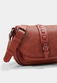 Červená texturovaná kožená crossbody taška s prohnutým klopem a nastavitelným popruhem. Obsahuje stříbrné kování a dekorativní akcent na popruhu.
