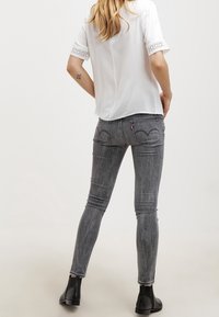 Jeans gris ajustados con textura desteñida y bolsillos traseros bordados, combinados con una camisa blanca con encaje en las mangas.