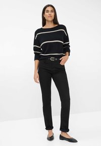 Jeans neri dal taglio dritto, abbinati a un maglione nero con righe orizzontali color crema. Accessoriato con una fibbia dorata per la cintura.