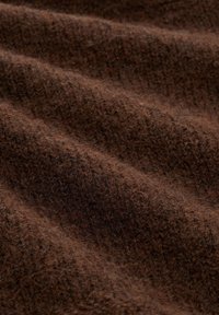 Brązowa wełniana tkanina o teksturowanym wykończeniu, z delikatnymi falami i różnymi odcieniami brązu, dodającymi głębi i ciepła. Miękka i gruba w wyglądzie.