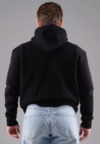 Schwarzer Kapuzenpullover mit gerippten Bündchen und Saum, getragen mit hellblauen Jeans, von hinten vor einem neutralen Hintergrund präsentiert.