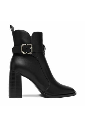 Bota de cuero negro hasta el tobillo con un tacón alto y ancho, puntera puntiaguda y una correa decorativa con hebilla plateada alrededor del tobillo.