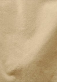 Tissu beige avec une légère texture de tissage diagonal et des plis subtils créant de douces ombres sur la surface.