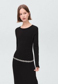 Robe noire côtelée à manches longues, dotée d'une ceinture en métal circulaire à la taille. Design minimaliste avec un décolleté rond.