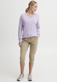 Lilla langermet V-hals genser kombinert med beige cropped joggebukser og grå joggesko. Løs passform med ribbestrikkede mansjetter og lommer.