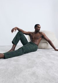 Zelené kockované nohavice vyrobené z jemného materiálu, s úzkym strihom a skrátenou dĺžkou, vystavené na postave bez trička na neutrálnom pozadí.