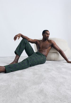 Pantaloni în carouri verzi, confecționați dintr-un material moale, cu un design slim-fit și lungime scurtă, expuși pe o figură fără tricou, pe un fundal neutru.