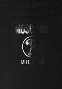 Svart bomullstyg med en glänsande silver "Moschino Milano"-logotyp och karaktärsdesign tryckt på fickan. Slät textur.